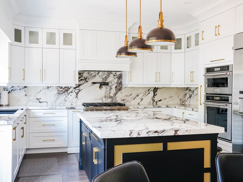 The Macchiato kitchen: white shaker cabinets, veined marble backsplash, brass-toned pendants and a navy island