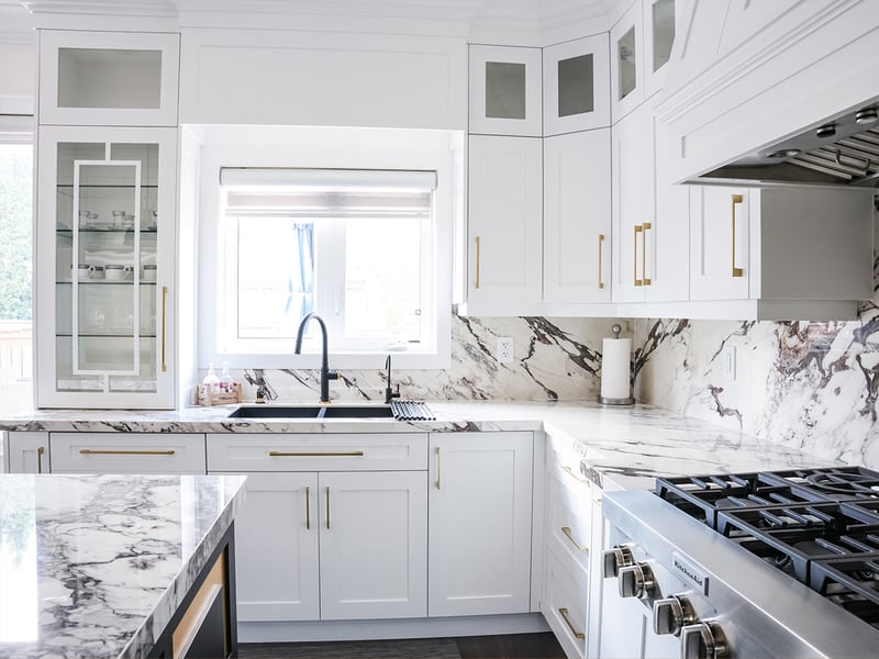 Sink wall with a window, black faucet and a full-height veined marble backsplash running on to the gas range